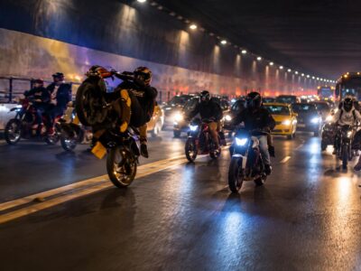 Motociclistas y otros vehículos dentro de un túnel iluminado durante la noche.