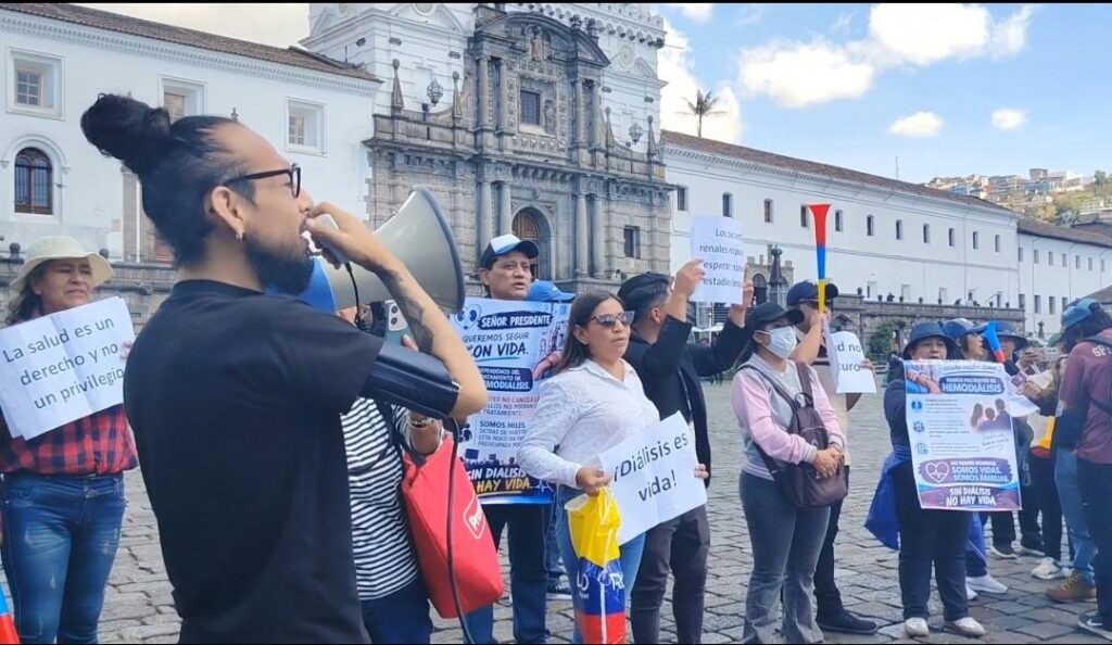 Manifestantes con carteles y un megáfono frente a un edificio del centro de Quito.
