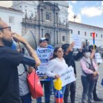Manifestantes con carteles y un megáfono frente a un edificio del centro de Quito.