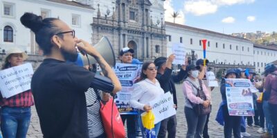 Manifestantes con carteles y un megáfono frente a un edificio del centro de Quito.