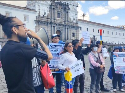Manifestantes con carteles y un megáfono frente a un edificio del centro de Quito.