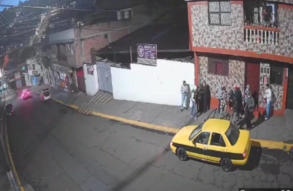 Captura de una cámara de seguridad con personas junto a un edificio y un taxi amarillo en la calle.