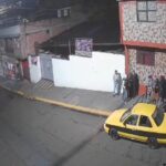 Captura de una cámara de seguridad con personas junto a un edificio y un taxi amarillo en la calle.