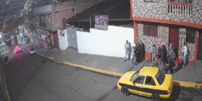 Captura de una cámara de seguridad con personas junto a un edificio y un taxi amarillo en la calle.
