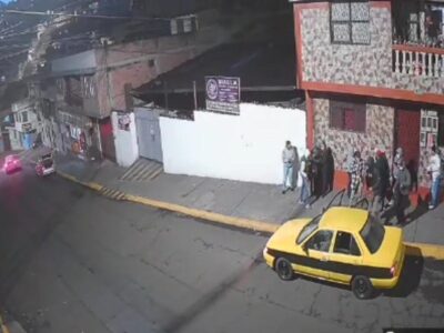 Captura de una cámara de seguridad con personas junto a un edificio y un taxi amarillo en la calle.