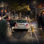Composición de un hombre con gorra en primer plano y personas junto a un automóvil en una calle nocturna.
