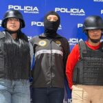 Agentes de Policía flanquean a dos mujeres con chalecos y cascos frente a un panel institucional.