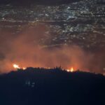 Llamas del incendio forestal en el caserío Apagua, parroquia Ambatillo, con la ciudad de Ambato iluminada al fondo, la noche del 6 de octubre de 2026.