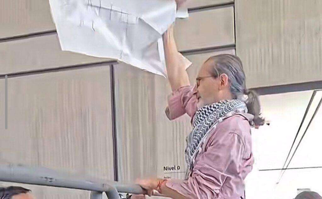 Santiago Rosano sostiene una pancarta junto a una barrera durante la protesta en la Universidad de Cuenca.