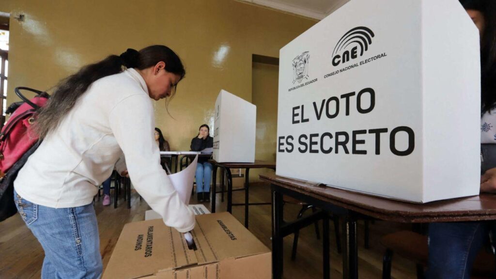 Una votante junto a una urna y un biombo del CNE con el texto «El voto es secreto».