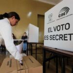 Una votante junto a una urna y un biombo del CNE con el texto «El voto es secreto».