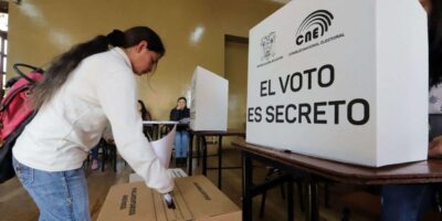 Una votante junto a una urna y un biombo del CNE con el texto «El voto es secreto».
