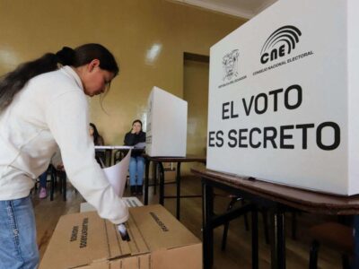 Una votante junto a una urna y un biombo del CNE con el texto «El voto es secreto».