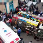Un vehículo de transporte volcado en una calle, rodeado de personas y una ambulancia.