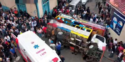 Un vehículo de transporte volcado en una calle, rodeado de personas y una ambulancia.