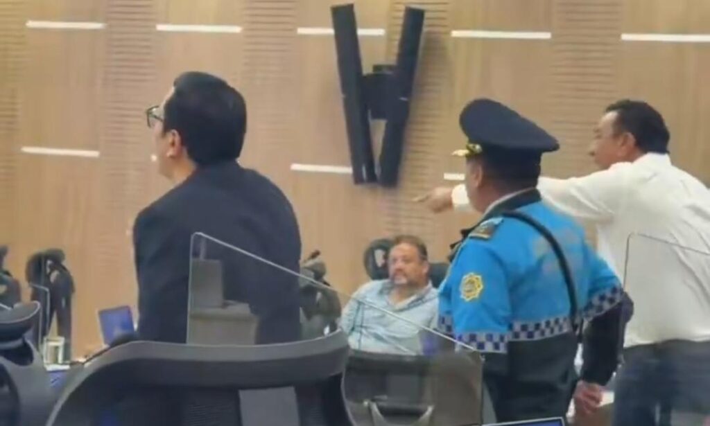 Un agente y varios hombres junto a las sillas de una sala de sesiones.