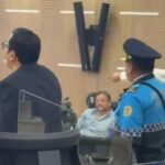 Un agente y varios hombres junto a las sillas de una sala de sesiones.