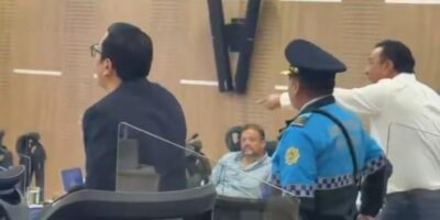 Un agente y varios hombres junto a las sillas de una sala de sesiones.