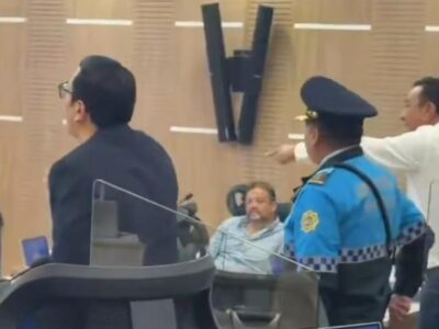 Un agente y varios hombres junto a las sillas de una sala de sesiones.