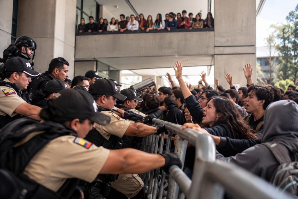 Policías y otras personas se encuentran a ambos lados de una barrera metálica durante una protesta.