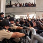 Policías y otras personas se encuentran a ambos lados de una barrera metálica durante una protesta.