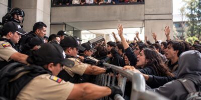 Policías y otras personas se encuentran a ambos lados de una barrera metálica durante una protesta.