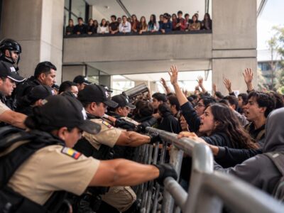 Policías y otras personas se encuentran a ambos lados de una barrera metálica durante una protesta.