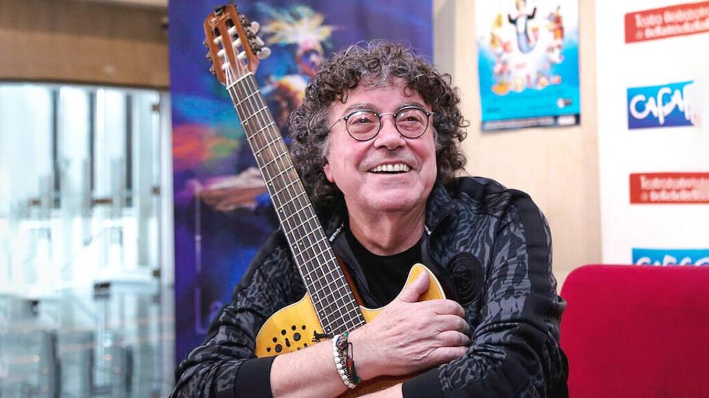 El cantante Piero sonríe mientras sostiene una guitarra durante una entrevista.