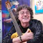 El cantante Piero sonríe mientras sostiene una guitarra durante una entrevista.
