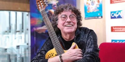 El cantante Piero sonríe mientras sostiene una guitarra durante una entrevista.