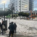 Personas caminan sobre una calle cubierta de granizo frente a edificios de Quito.