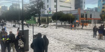 Personas caminan sobre una calle cubierta de granizo frente a edificios de Quito.