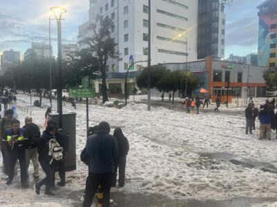 Personas caminan sobre una calle cubierta de granizo frente a edificios de Quito.