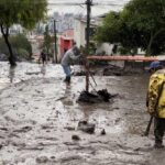 Personas trabajan con palas en una calle cubierta de lodo y escombros.