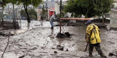 Personas trabajan con palas en una calle cubierta de lodo y escombros.
