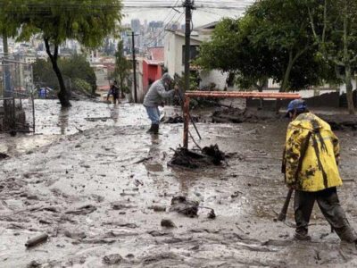 Personas trabajan con palas en una calle cubierta de lodo y escombros.