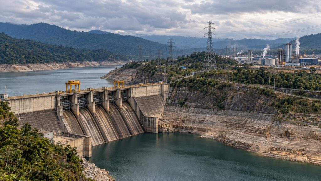 Imagen ilustrativa de una represa con bajo nivel de agua, torres eléctricas y un complejo industrial al fondo.