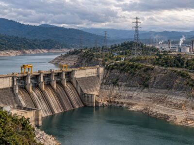 Imagen ilustrativa de una represa con bajo nivel de agua, torres eléctricas y un complejo industrial al fondo.