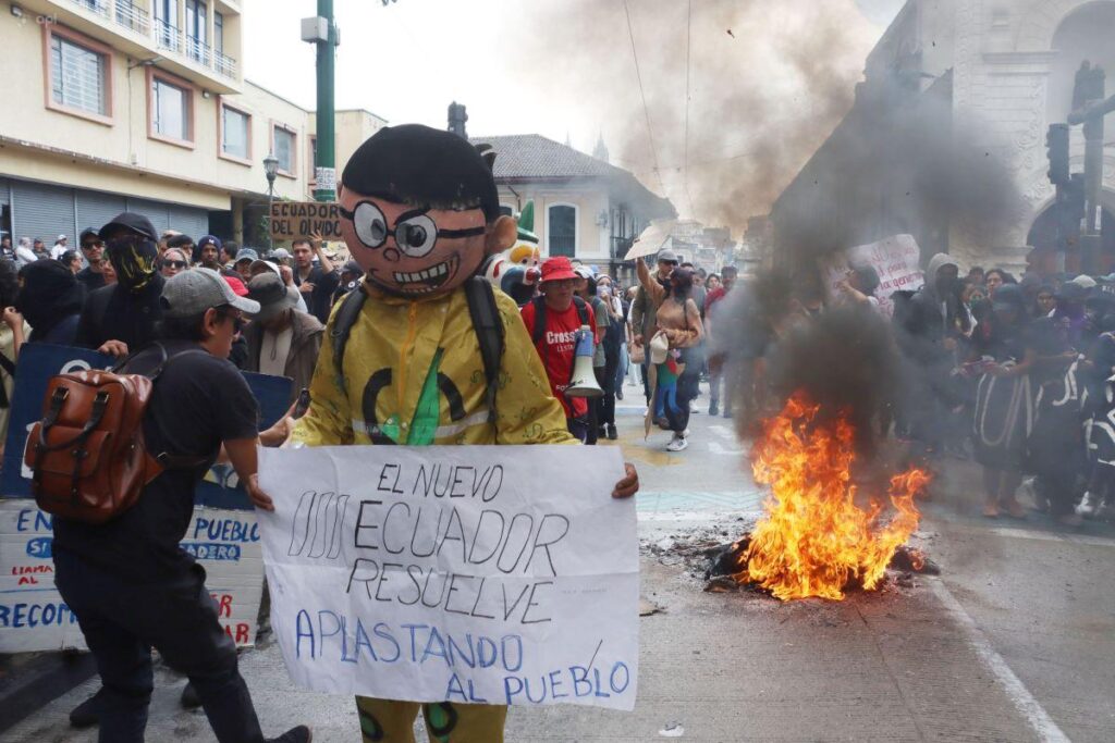 Manifestantes sostienen una pancarta y un muñeco junto a una quema en la calle