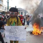 Manifestantes sostienen una pancarta y un muñeco junto a una quema en la calle