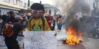 Manifestantes sostienen una pancarta y un muñeco junto a una quema en la calle