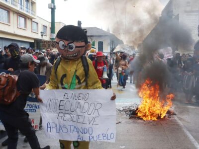 Manifestantes sostienen una pancarta y un muñeco junto a una quema en la calle